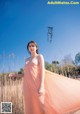 A woman in a long pink dress standing in a field.