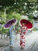 Two women in kimonos standing next to each other holding umbrellas.